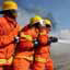 Three men in orange firefighting uniforms and hardhats holding a hose spraying water