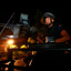 Black helmeted soldier standing through the roof opening of a military vehicle riding through a lamp lit street