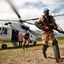 Soldier wearing khaki uniform holds a rifle moves away from a while helicopter