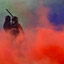 Two figures are seen behind red, green and purple smoke