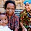 Smiling woman in military uniform sits between two smiling woman, one holding a child