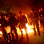 Silhouettes of several rows of uniformed men carrying shields with fire around them