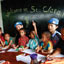 Three uniformed women sit with five young children in front of a black board that reads 