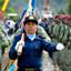 Blue-uniformed officer carries a the flag leading two lines of green-uniformed soldiers