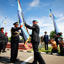 Blue uniformed officer hands a blue flag to another uniformed officer with photographers takin g picture