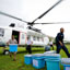 Three blue boxes sit on open field while a man carries a fourth from a white UN helicopter