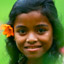 Girl with flower on ear against a green background smiles at the camera